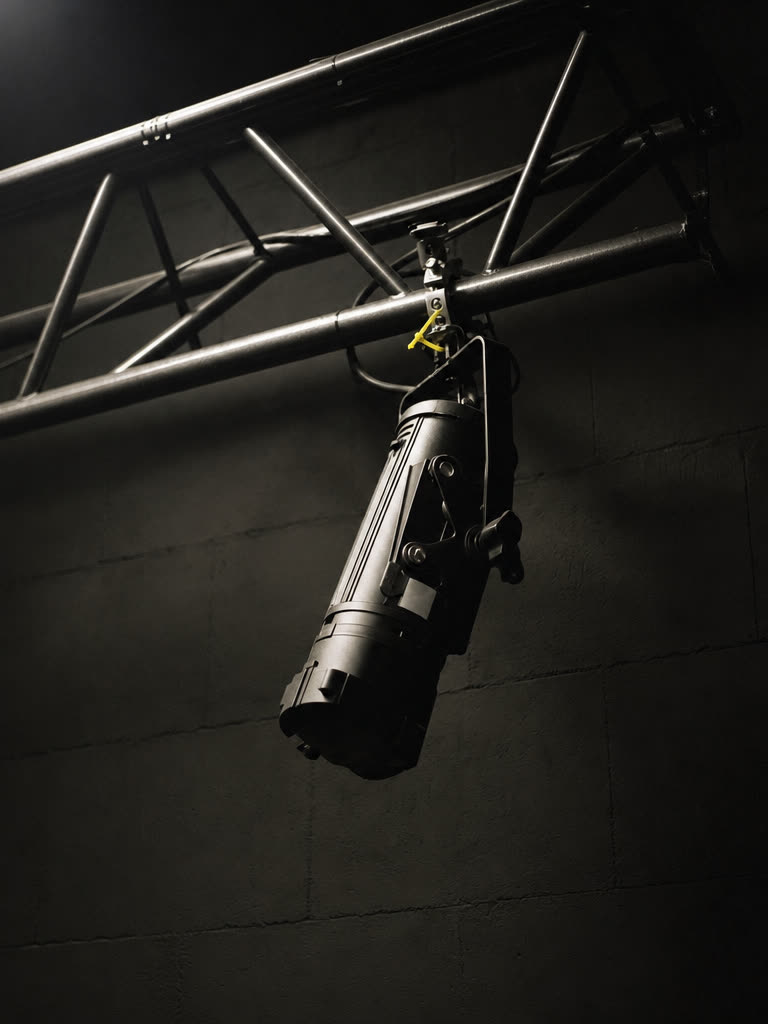 A section of black aluminium truss with one unlit stage fixture hung from it against a dark wall
